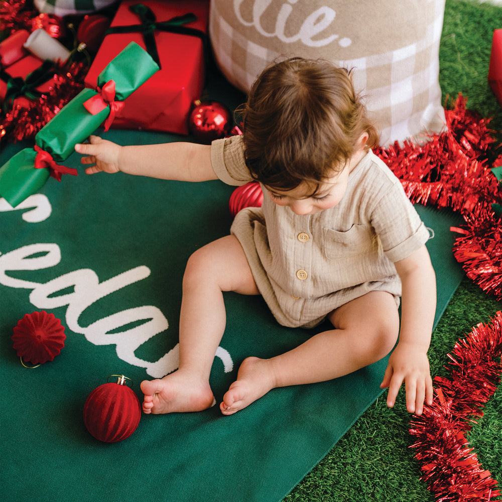 Child playing with Christmas decorations on a green blanket with red tinsel.