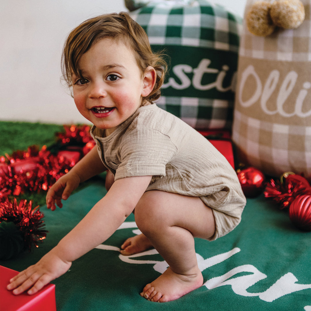 Child playing with christmas decorations on a green blanket with checkered santa sacks in background.