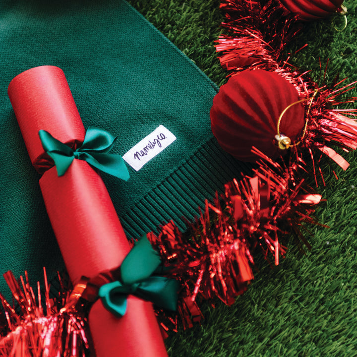 Green knitted blanket with red cracker and tinsel on a grassy background
