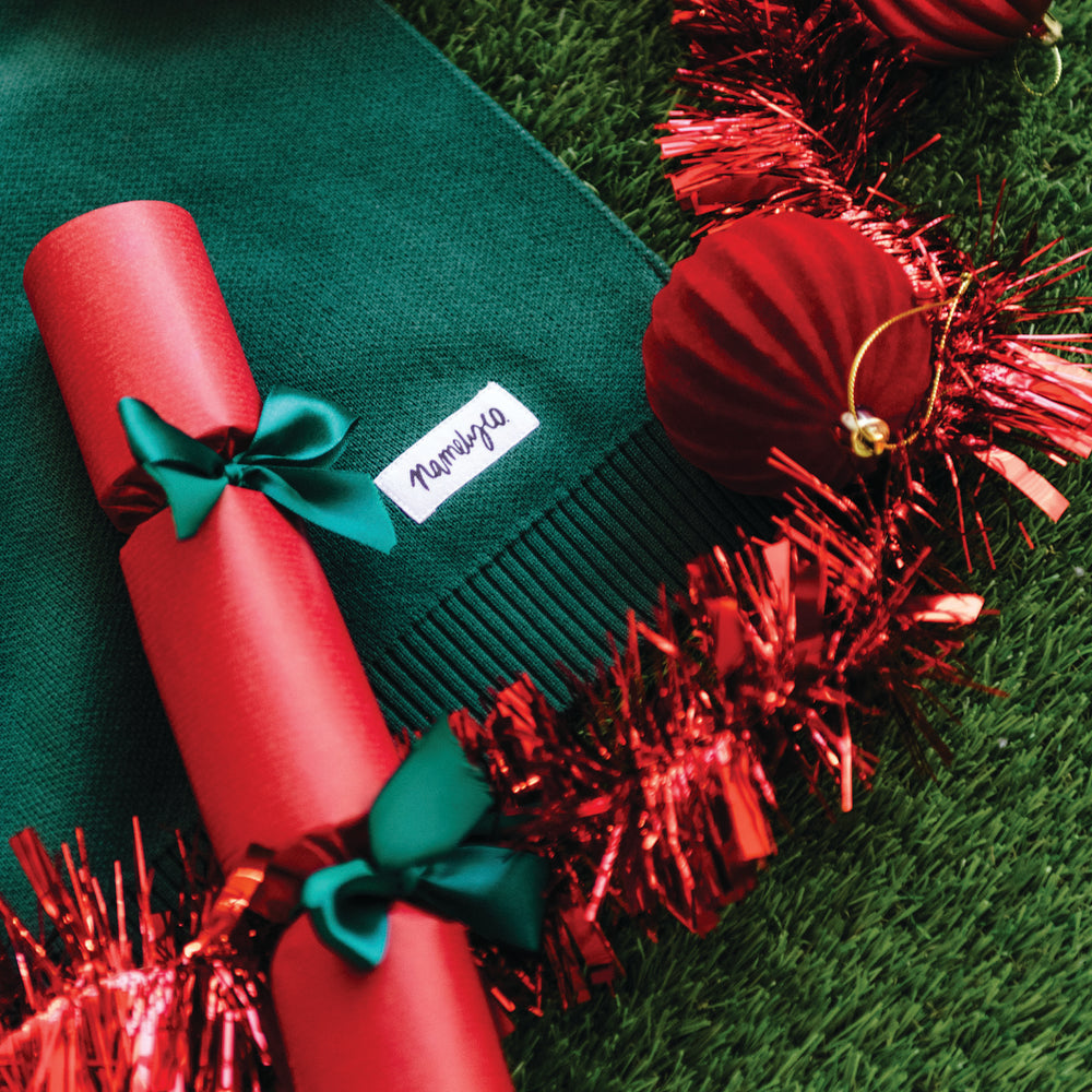 
                  
                    Load image into Gallery viewer, Green knitted blanket with red cracker and tinsel on a grassy background
                  
                